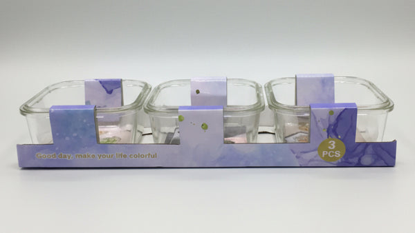 Set of three glass containers with purple lids in packaging on a white background